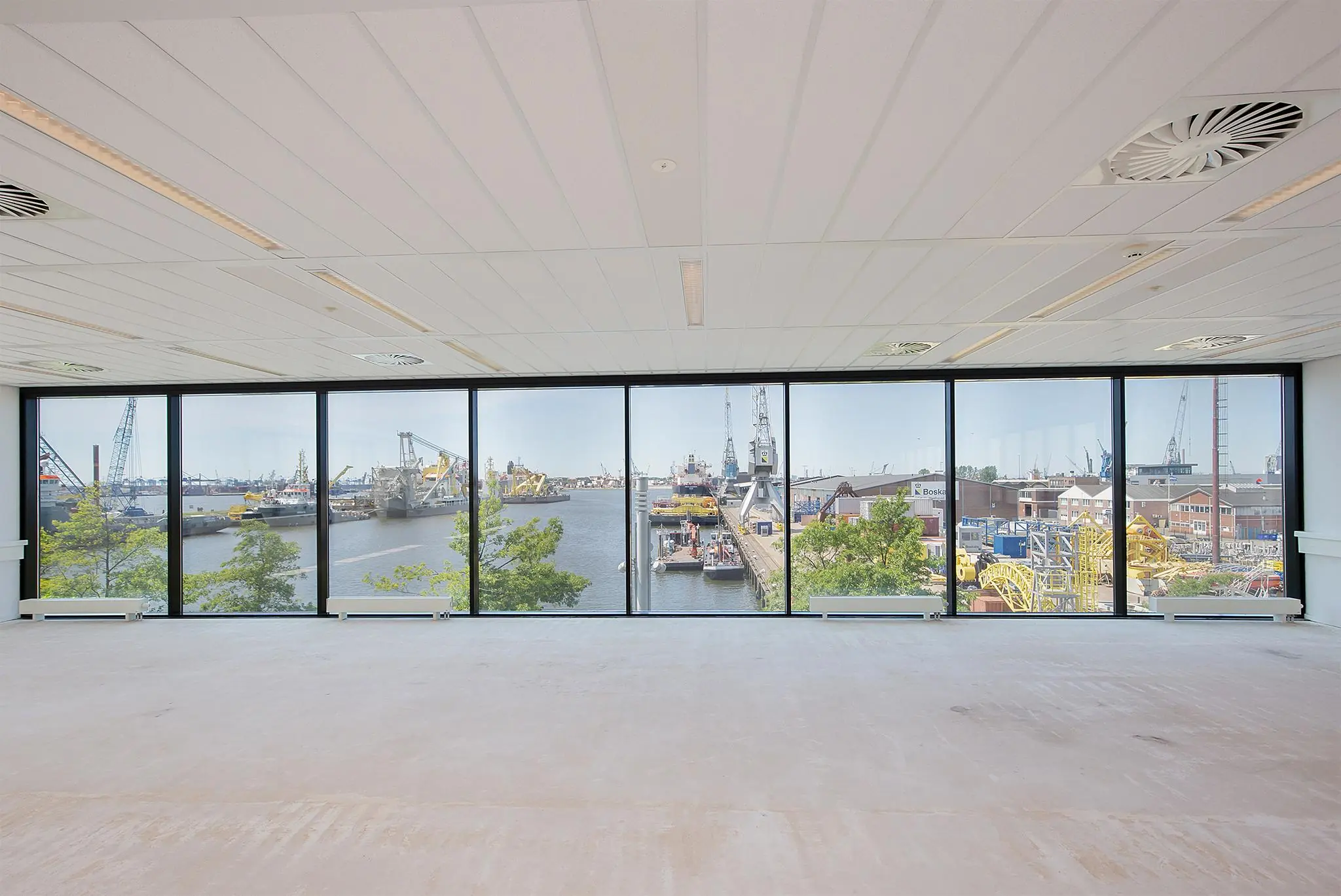 Uitzicht vanuit een leeg kantoor op de Waalhaven in Rotterdam met schepen, kranen en havenactiviteiten.